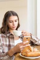 Woman looking for information on Internet, using mobile, during eating breakfast. Concept photo
