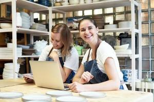 dos empresarias sonrientes con laptop en un taller artesanal. retrato de mujer sonriente alegre foto