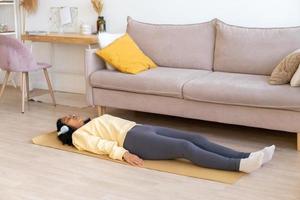 African-american female lying on mat in living room. Relaxing after doing workout in headphones photo