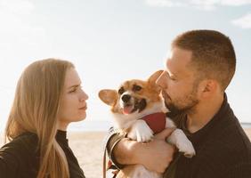 joven pareja feliz con perro toma selfie en la playa. hermosa chica y chico y cachorro corgi foto
