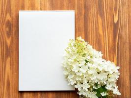 Billboard with blank sheet for notes and white flower hydrangeain abstract blank wooden background. Notebook with empty space. photo