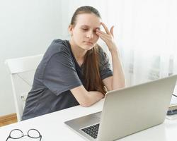 Girl rubs her eyes, her eyes are tired from strain and hurt. Concept of harmful effects of computer photo