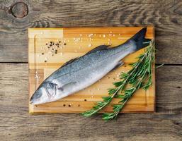 fresh, raw, saltwater fish, sea bass on a wooden cutting board on old wooden aged, rustic table, top view photo