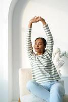 Young african-american female stretching while sitting. Thougtfuly looking at window in morning photo