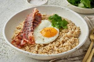 Oatmeal, fried egg, fried bacon. Hearty fat high-calorie breakfast. Balance of proteins, fats, carbohydrates, side view photo