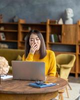 Asian woman yawning due to overworking and exhausting. Young lady in bright yellow jumper photo