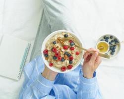 Top view faceless woman holding plate of oatmeal, sitting in bed early morning photo