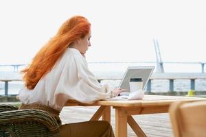 Redhead woman typing on laptop in outdoors cafe photo