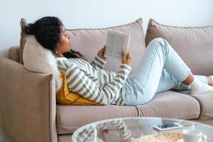 mujer afroamericana descansando en el sofá y leyendo un libro. estar desconectado para la desintoxicación digital foto