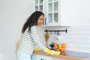 mujer afroamericana con guantes de goma ocupada con tareas domésticas en la cocina foto