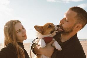 joven pareja feliz con perro tomando foto selfie en la playa. hermosa familia y cachorro corgi