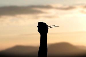 silhouette of a human hand holding a cross held up in the sky. sunset background photo