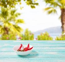 Decoration of red hot chili pepper on blue wodden board on blurred beach background. Set,copy space,mock up. Cayenne on white plate