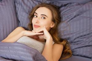 Portrait pretty young white girl on bed in modern apartment in the morning. She keeps eyes opened and looks satisfied. Beautiful young woman basking in bed in the morning. Beautiful Model face photo