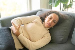 mujer latina, acostado, en, sofá, con, dolor de estómago, sensación