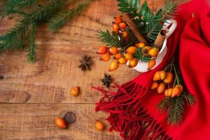 Winter, warm atmosphere. A composition with a cup with spruce branches and rosehips on a wooden background