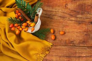 Winter, warm atmosphere. A composition with a cup with spruce branches, rosehips and yellow scarf on a wooden background photo