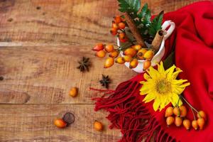 Composition with a cup with rose berries, spruce branches and a red scarf with sunflower on a wooden background photo