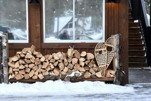 firewood and snow shoes sit outside a cabin