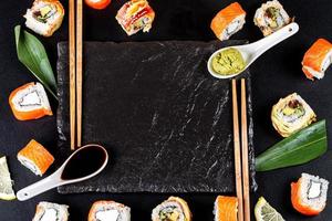 Japanese food frame with different sushi, sauces and chopsticks on black background, top view