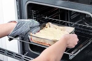 A woman puts a raw pie in an open electric oven