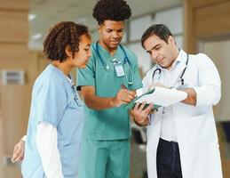 los estudiantes de medicina afroamericanos están aprendiendo con un médico profesional en el hospital de la escuela de medicina. un joven médico interno sostiene un portapapeles en la capacitación laboral con el maestro médico foto