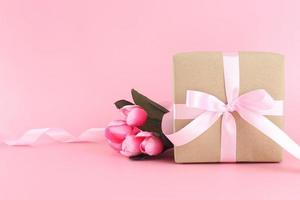 caja de regalo de papel marrón con lazo de cinta rizada de satén rosa sobre fondo rosa pastel. Flat lay día de la madre, día del padre, día de san valentín, conceptos de cumpleaños con espacio de copia. foto