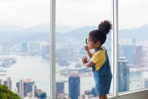 Little child girl with magnifying glass looking outside through the window, Kid standing and looking through the window with clipping path photo