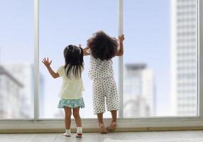 Two little girl looking outside through the window, View form behind of kids standing and looking through the window with clipping path photo