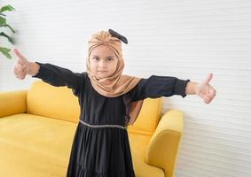 Cheerful kid girl showing thumbs up, portrait of pretty muslim child girl with hijab showing double thumb up and looking at camera photo