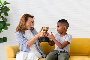 Kid boy carry trophy with mom, little boy congratulations grandmother and gives trophy at home photo