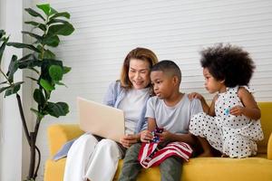 Children and grandmother playing cheerfully in living room, Mother and little children sitting on couch using laptop, boy holding usa flag photo