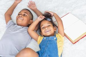 retrato en ángulo alto de dos niños acostados en el suelo blanco y mirando a la cámara, hermana feliz y hermano jugando en la sala de estar foto