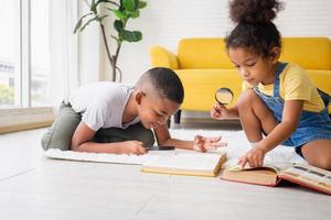 hermano y hermana encontrando una palabra en el libro con lupa en el suelo, niños felices jugando en la sala de estar foto