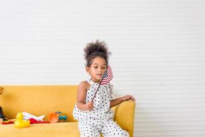 Cute little girl with a small national flag of United States, kid girl playing in living room