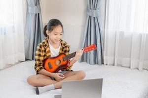 niña toca la guitarra, niña aprendiendo a tocar la guitarra en el dormitorio, hobby para niños