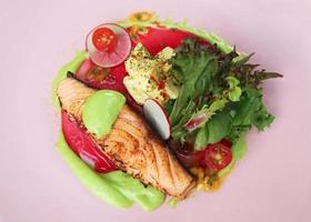 Grilled salmon fillet, slow cooked steak with wasabi cream sauce, radish, tomato and passionfruit served with potato salad on isolated pink background. Healty food concept