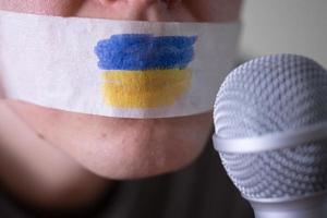 Tape over his mouth with the flag of Ukraine, trying to speak into a microphone. photo