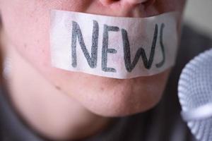 A man gags his mouth with duct tape saying news trying to speak into a microphone. photo