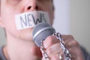 A man gags his mouth with duct tape saying news trying to speak into a microphone. photo