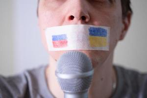 A duct-taped mouth with a flag of Russia and Ukraine trying to speak into a microphone. photo