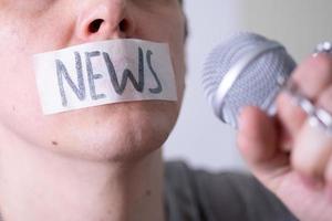 un hombre se amordaza la boca con cinta adhesiva diciendo noticias tratando de hablar por un micrófono. foto