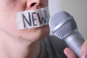 A man gags his mouth with duct tape saying news trying to speak into a microphone. photo