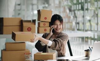 Happy young Asian woman entrepreneur, Smile for sales success after checking order from online shopping store in a smartphone at home office, Concept of merchant business online and eCommerce
