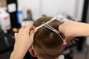 niño pequeño con una máscara, que se corta en la barbería en la barbería, corte de pelo elegante y de moda para un niño. foto