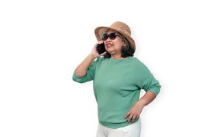 Portrait of happy asian senior woman wearing sunglasses, a hat, and holding smartphone standing isolated on white background. Concept of tourist enjoy and fun valentine day after retire photo