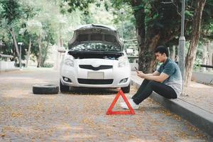 Asian man using smartphone for assistance after a car breakdown on street. Concept of vehicle engine problem or accident and emergency help from Professional mechanic photo