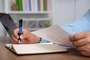 Asian Businessman Writing a business plan After looking at the annual profit and loss summary report.  The concept of Business success Needs to be analyzed And management planning. photo