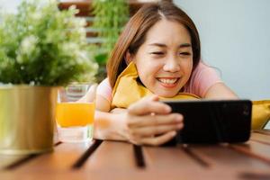 Happy Asian woman sitting in the backyard and holding smartphone for watching a movie series during relax time. photo