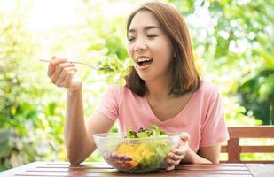 The happy beautiful Asian healthy middle aged woman sitting in the balcony of the house beside the garden and eat a healthy green salad. Concept of health care and nutritious food photo